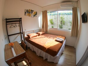 A bedroom with a bed, a desk, a chair, a window with curtains, and a wall-mounted TV.