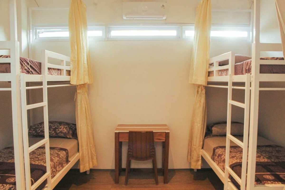 A dormitory room with bunk beds, a small desk, and a window.