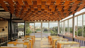 A dining area with wooden tables and chairs, large windows offering a view of the cityscape.