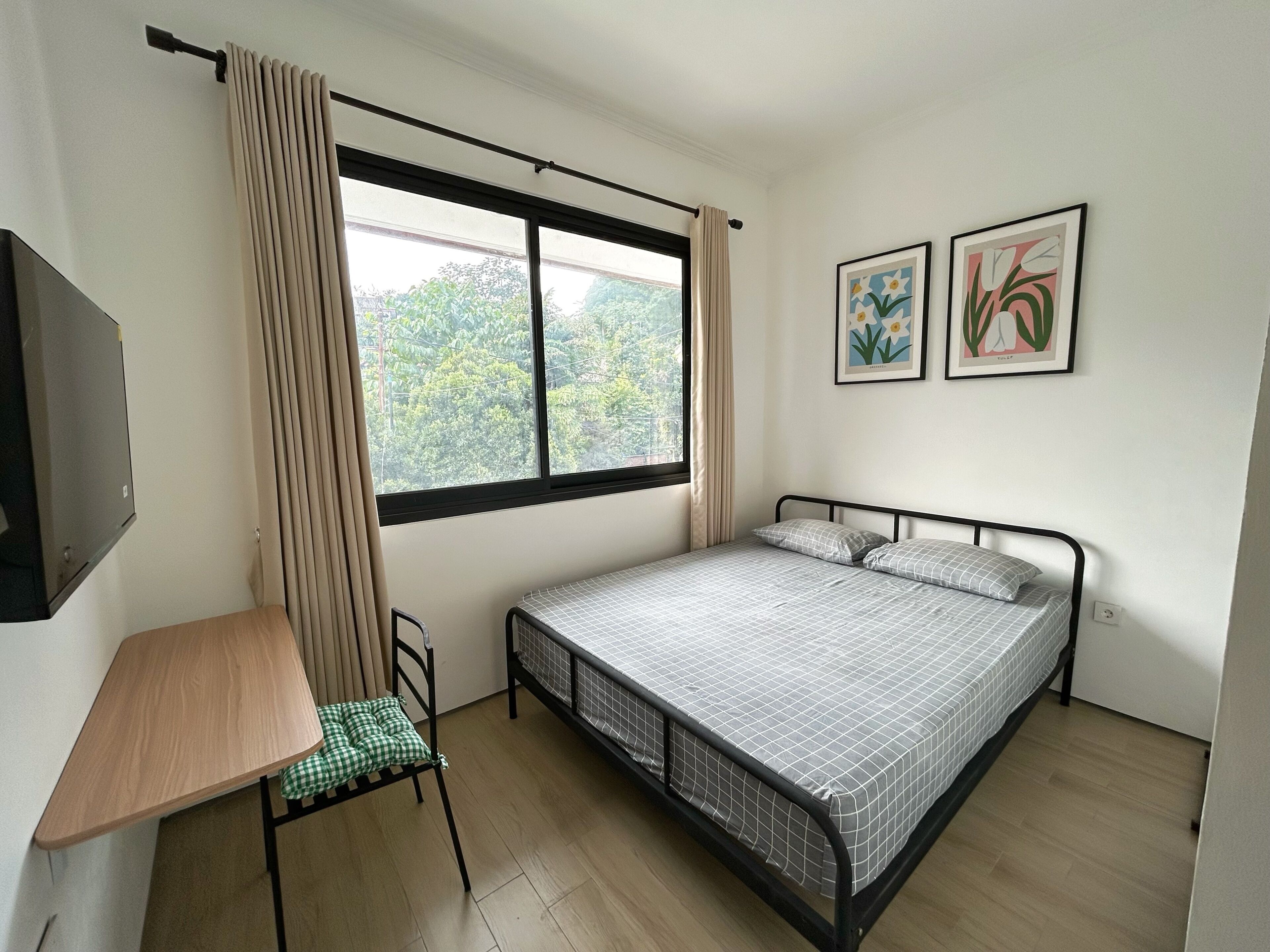 A bedroom with a bed, a desk, a chair, a window with curtains, and two wall-mounted pictures.