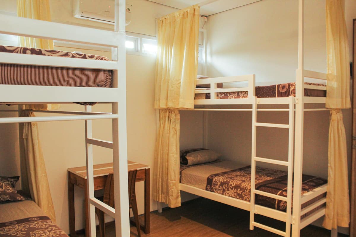 A dormitory room with bunk beds, a wooden desk, and a chair.