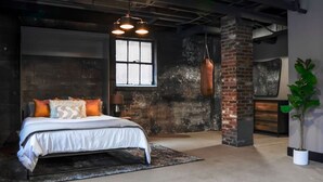 A bedroom with a bed, a hanging punching bag, a window, and a brick wall.