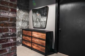 Una habitación con pared de ladrillo, un mueble de madera con cajones, una puerta negra y una obra de arte con textura en la pared.