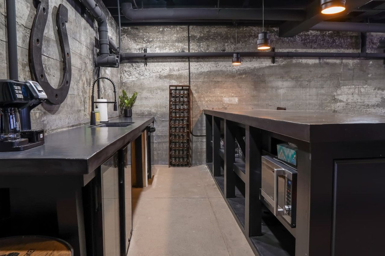 A narrow kitchen with a concrete wall, a coffee machine, and a wine rack.
