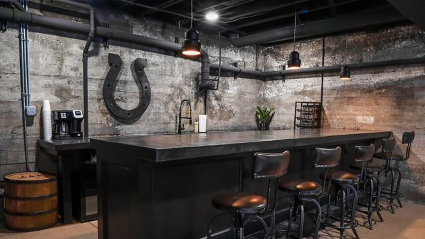 A bar area with a black bar counter, stools, and a large horseshoe-shaped metal object on the wall.