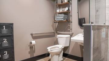 A bathroom with a toilet, a sink, a mirror, a shelf with toiletries, and a storage unit with numbered drawers.