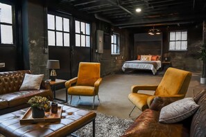 Una habitación amplia con una cama grande, dos sillones, un sofá de cuero y una mesita con una bandeja.