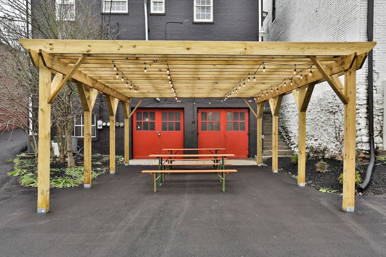 A wooden pergola structure with a bench underneath, red doors, and string lights.