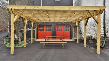 A wooden pergola structure with a bench underneath, red doors, and string lights.