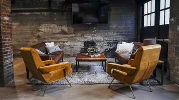 Un rincón acogedor con dos sillones de cuero y una mesa de centro de madera, frente a una pared de ladrillo rústico con un ventanal grande y un televisor.
