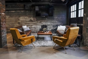 A cozy seating area with two leather armchairs and a wooden coffee table, set against a rustic brick wall with a television mounted above.