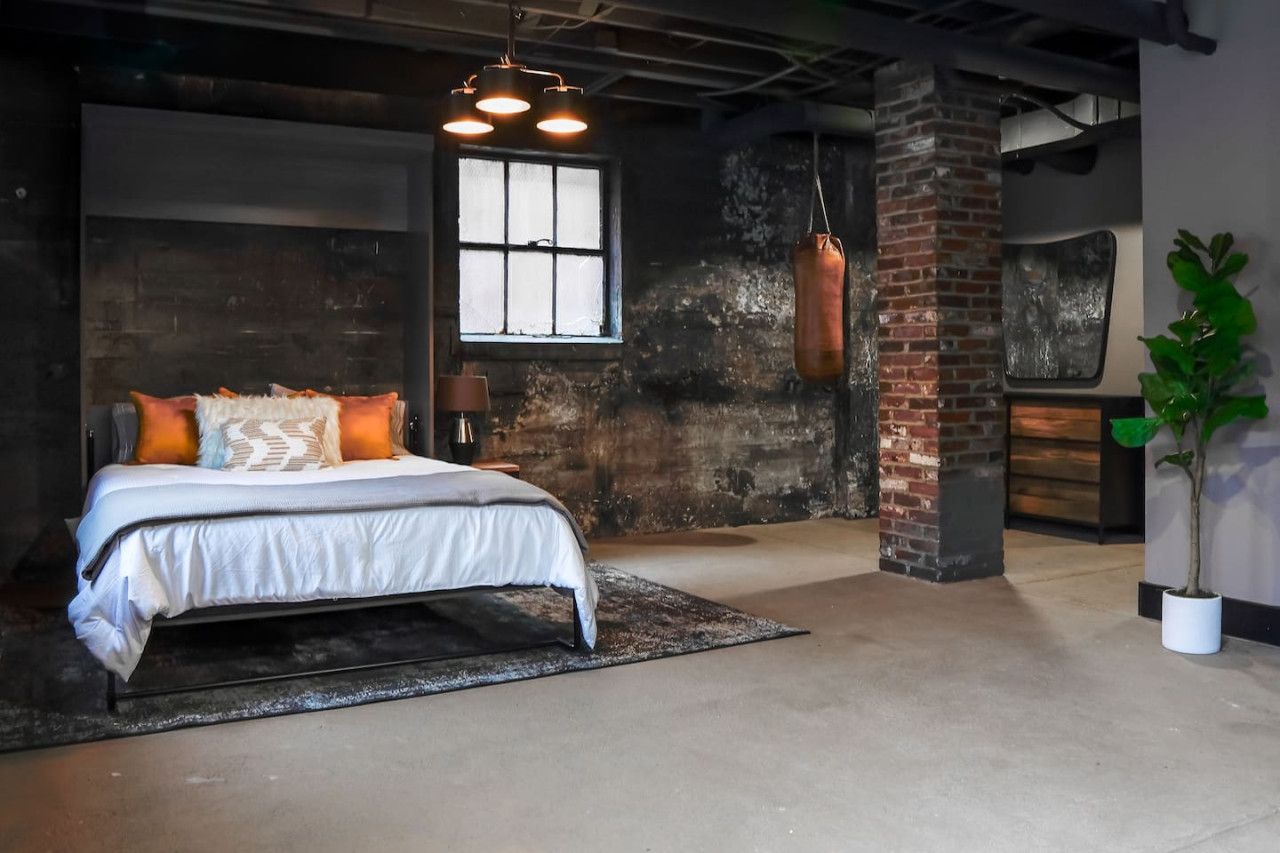 A bedroom with a bed, a hanging punching bag, a window, and a brick wall.