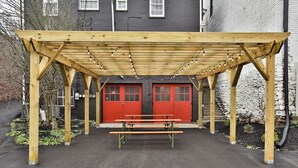 A wooden pergola structure with a bench underneath, red doors, and string lights.