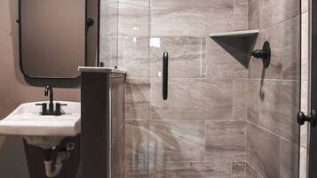 A modern bathroom with a glass-enclosed shower, a pedestal sink, and a wall-mounted mirror.