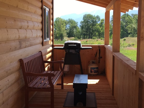 A wooden deck with a bench and a grill, overlooking a grassy landscape.