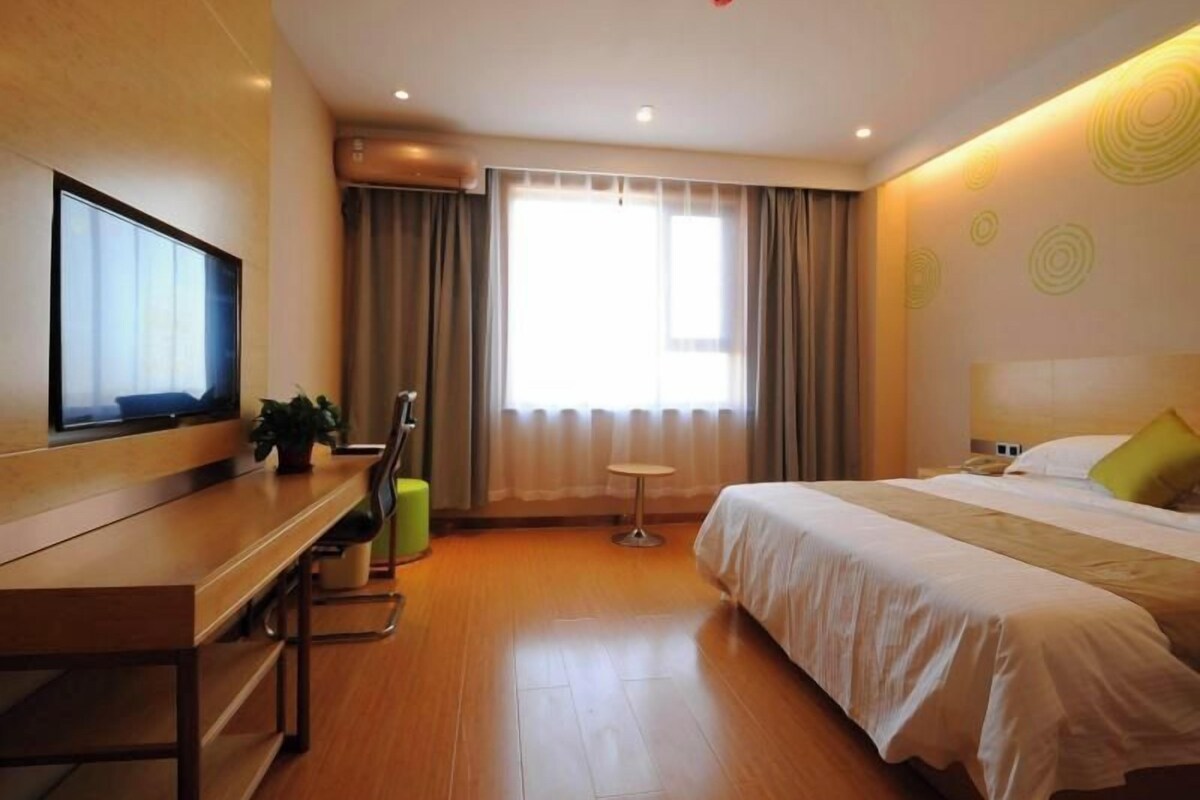 Een hotelkamer met een bed, een bureau met stoel, een televisie en een raam met gordijnen.