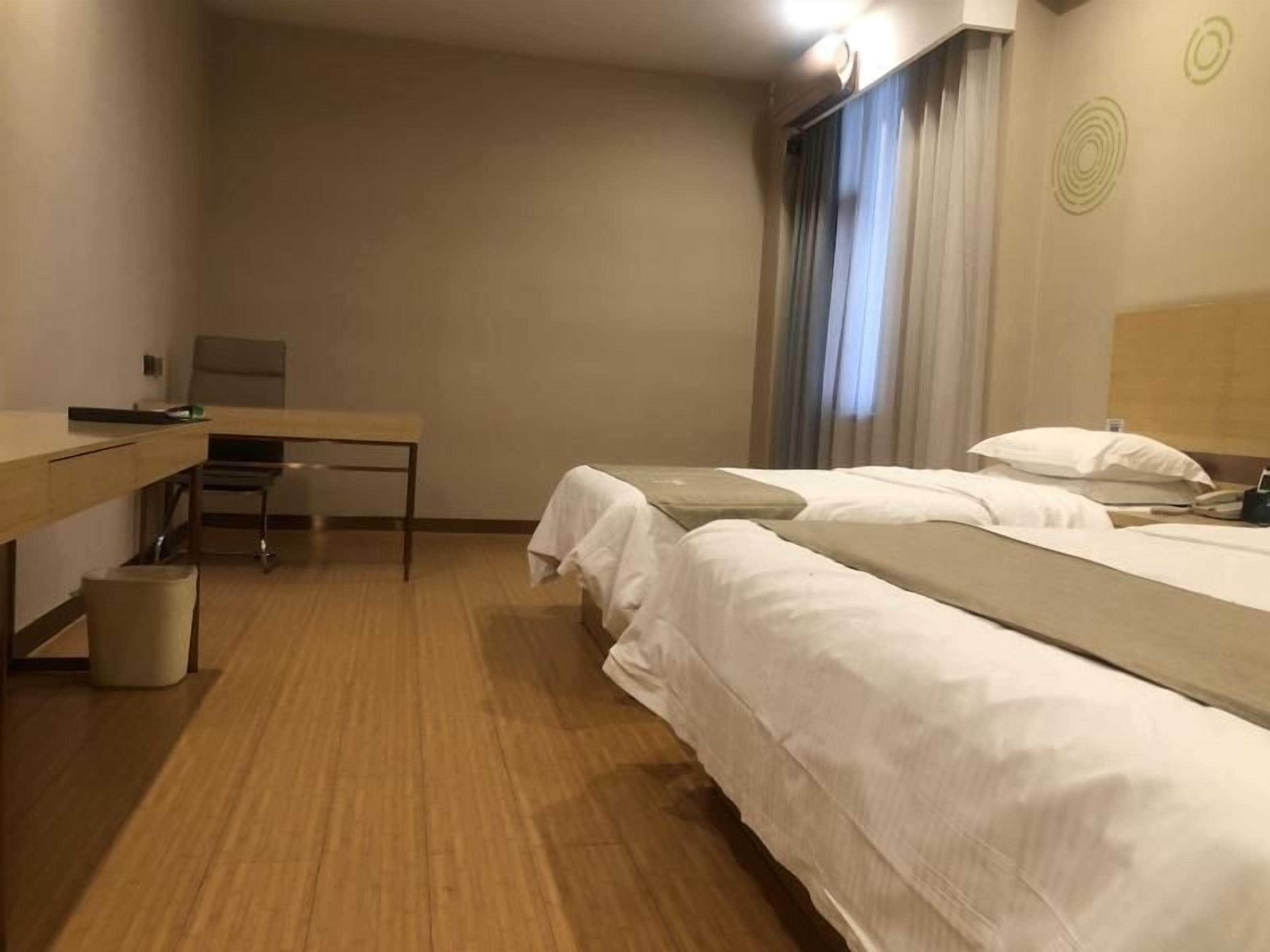 A hotel room with two beds, a desk, a chair, and a trash bin.