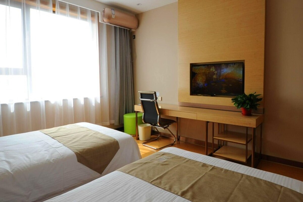 Een hotelkamer met twee bedden, een bureau met stoel, een televisie en een raam met gordijnen.