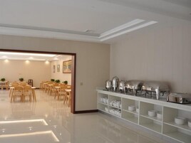 Un comedor amplio con mesas y sillas de madera, una barra de buffet con cubiertos, y un interior limpio y moderno.