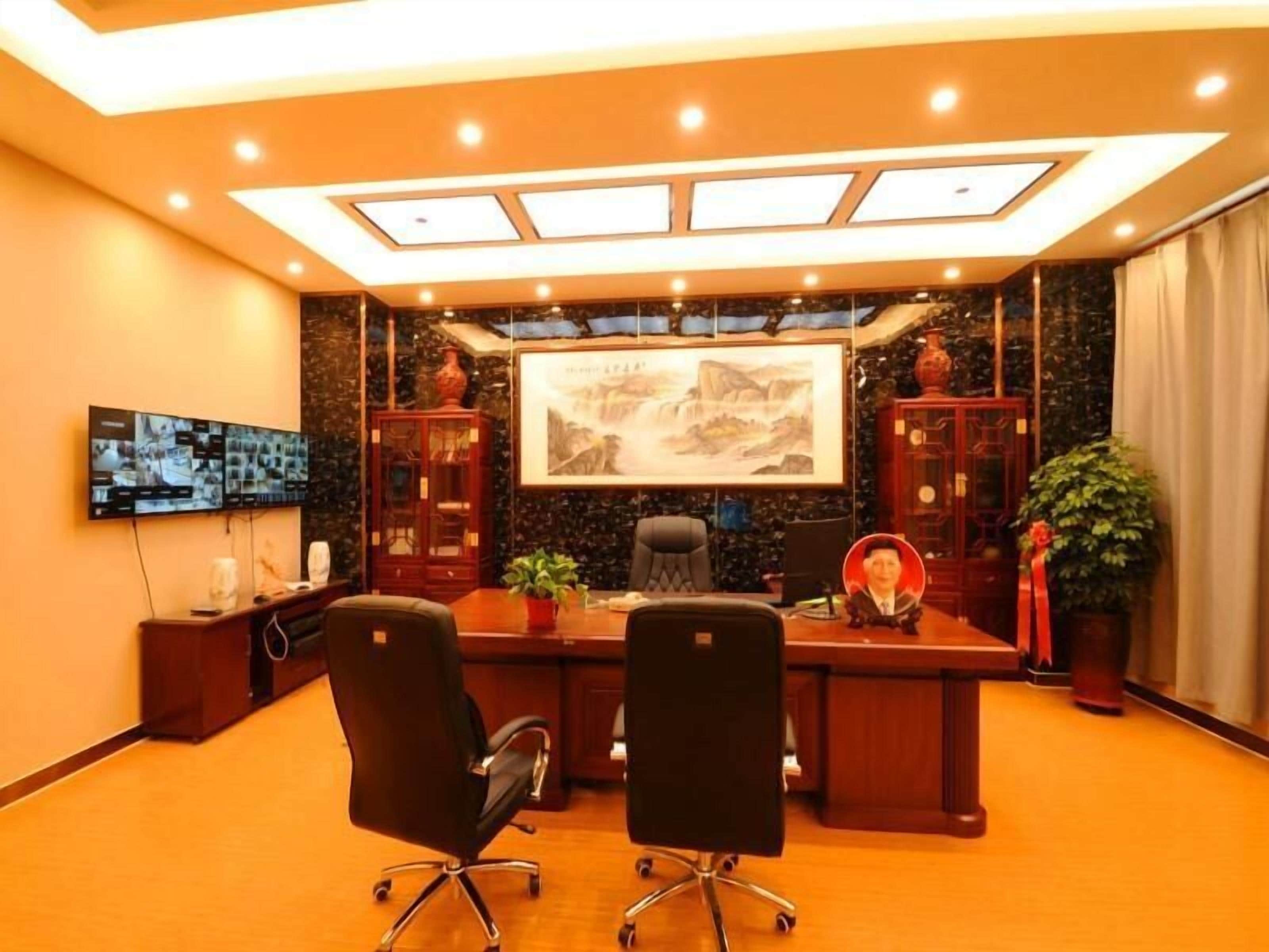 A conference room with a large desk, two office chairs, a television mounted on the wall, and a large framed painting.