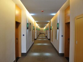 Un largo y estrecho pasillo de hotel con puertas a ambos lados, cada una señalizada con un letrero verde de salida.