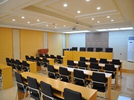 Un salón de conferencias con filas de mesas y sillas, un atril y una pantalla de proyector.