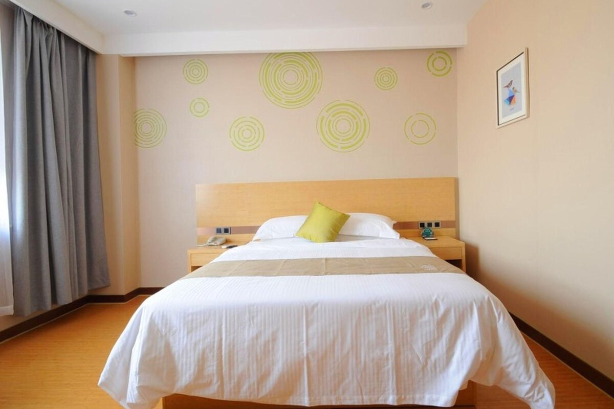 Een hotelkamer met een groot bed, een houten hoofdbord, een nachtkastje met een telefoon en een wand met cirkelmotieven.