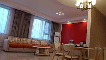 A modern living room with a sofa, a dining table with chairs, a chandelier, and a red accent wall.