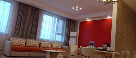 A modern living room with a sofa, a dining table with chairs, a chandelier, and a red accent wall.