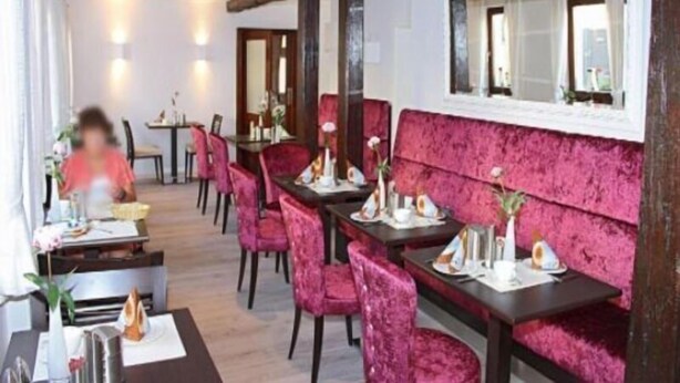 A dining area with tables and chairs, a mirror on the wall, and a window with a view. - Haus Anna An Der Stadtmauer (Hanau)