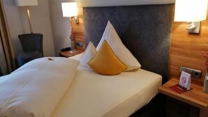 A hotel room with a neatly made bed, a wooden headboard, two bedside tables with lamps, and a chair. - Haus Anna An Der Stadtmauer (Hanau)