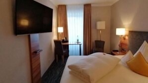 A hotel room with a bed, a desk, a chair, a TV, and a window with curtains. - Haus Anna An Der Stadtmauer (Hanau)