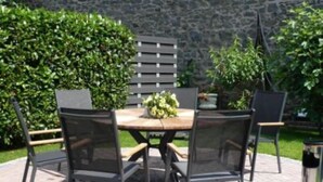 An outdoor seating area with a round table and chairs, surrounded by greenery and a stone wall. - Haus Anna An Der Stadtmauer (Hanau)