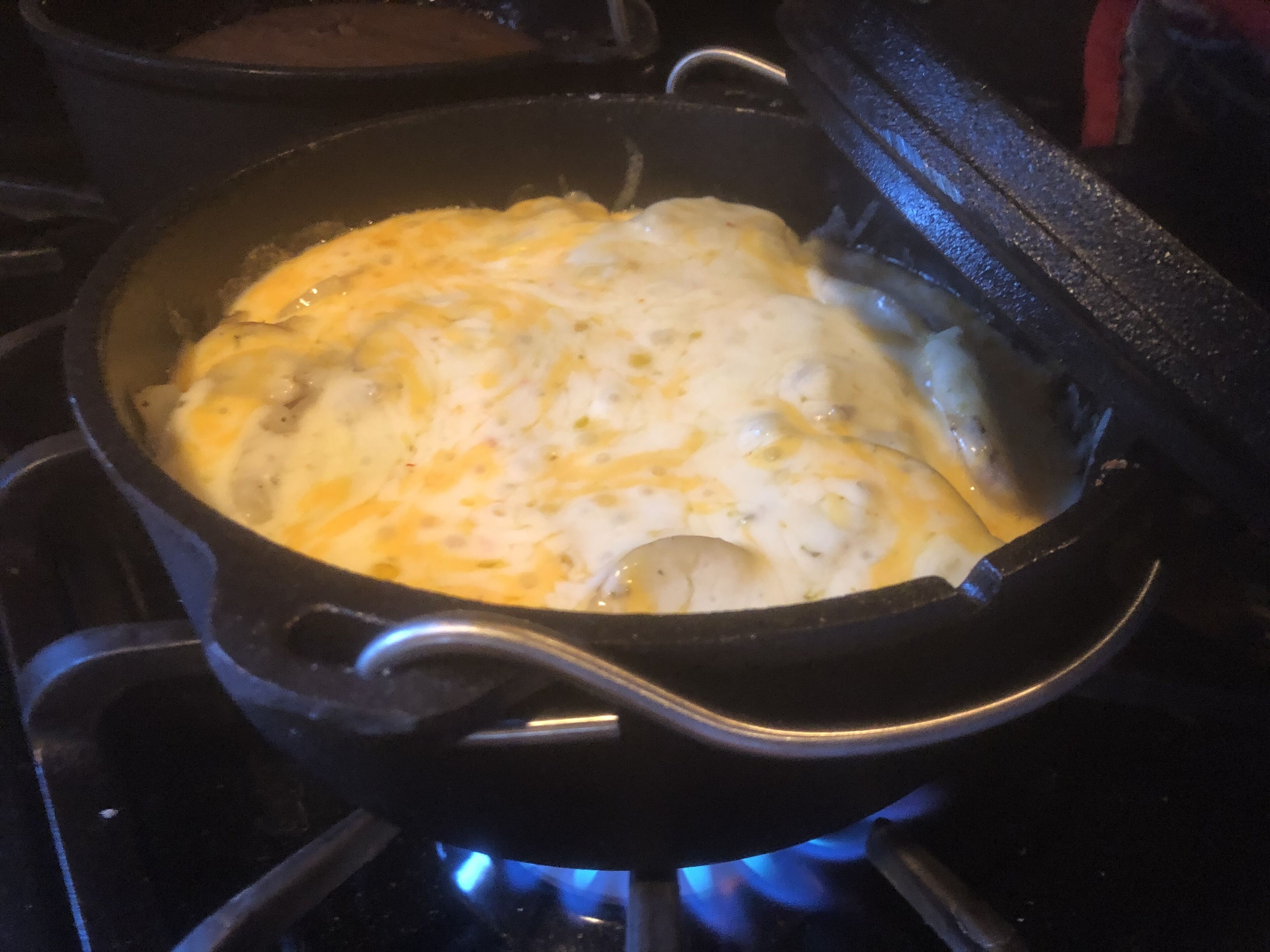 Une casserole noire sur une cuisinière, avec une flamme bleue en dessous.