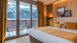 A hotel room with a large bed, a balcony with chairs, and a mountain view. - La Rosiere (Montvalezan)