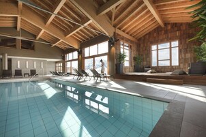 Una piscina interior con vigas de madera, ventanas amplias y sillones de descanso.