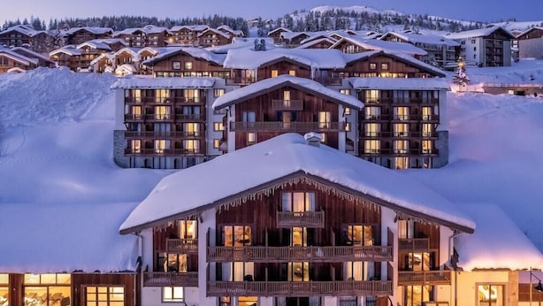 A multi-story lodge with balconies and large windows, surrounded by snow-covered buildings and a mountainous backdrop. - La Rosiere (Montvalezan)