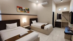 A hotel room with two beds, a painting on the wall, an air conditioning unit, a small desk with a mirror, and a bathroom with a sink and shower. - Hotel Orizatha (Mataram)