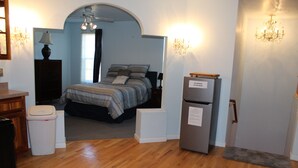 Un dormitorio con cama, refrigerador, escritorio y un cubo de basura.