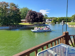 A boat with passengers on a river, surrounded by greenery and houses.