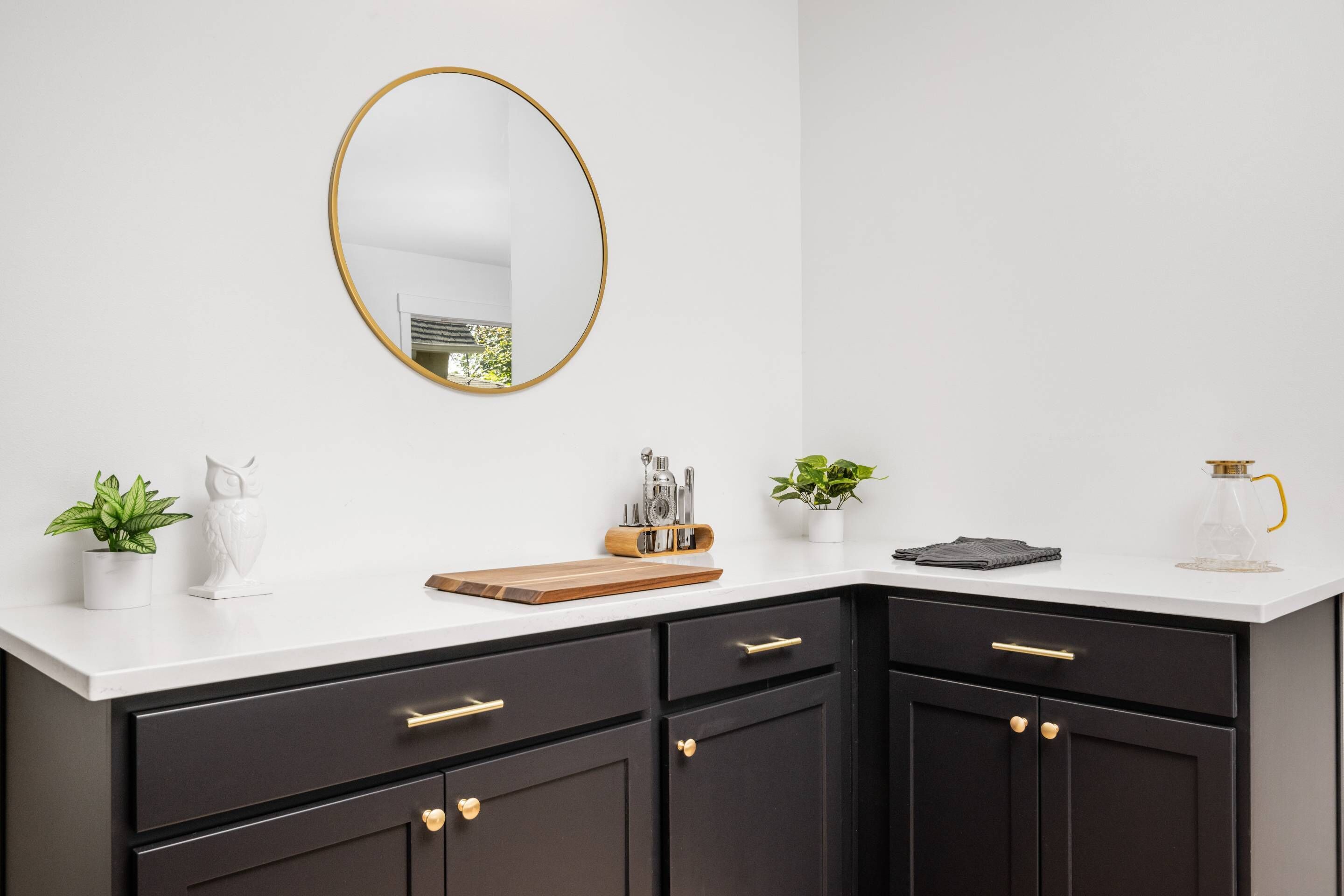 A modern kitchen with dark cabinets, a white countertop, a gold-framed mirror, and various kitchen items.