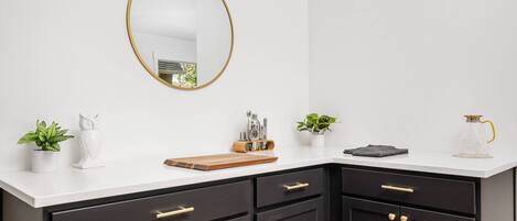 A modern kitchen with dark cabinets, a white countertop, a gold-framed mirror, and various kitchen items.