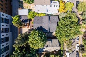 An aerial view of a residential area with multiple buildings, including a two-story house with a sloped roof and a flat-roofed structure. - Pristine Renovation w/ Epic Location, Pet Friendly, Fully Fenced, Hot Tub, Walk to Bars, Shopping (Portland)