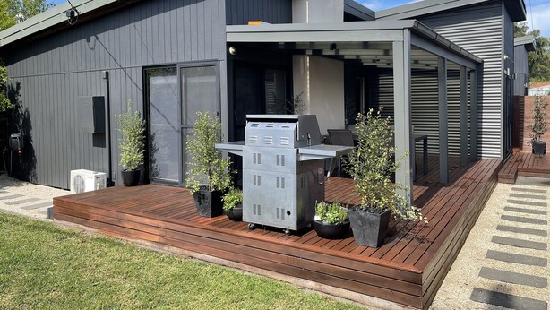 Un edificio moderno con un patio cubierto, asientos exteriores y plantas en macetas.
