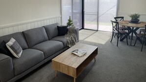 Una sala de estar moderna con un sofá gris, una mesa de centro de madera y un comedor con mesa y sillas.