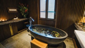 A modern bathroom with a freestanding bathtub, wooden paneling, a window, and a small plant. - JSI Resort (Megamendung)