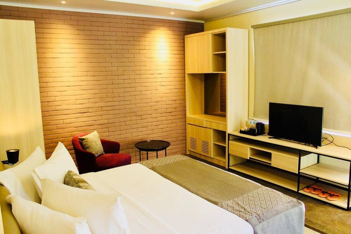 A hotel room with a bed, a red chair, a small table, a TV, and a wardrobe.