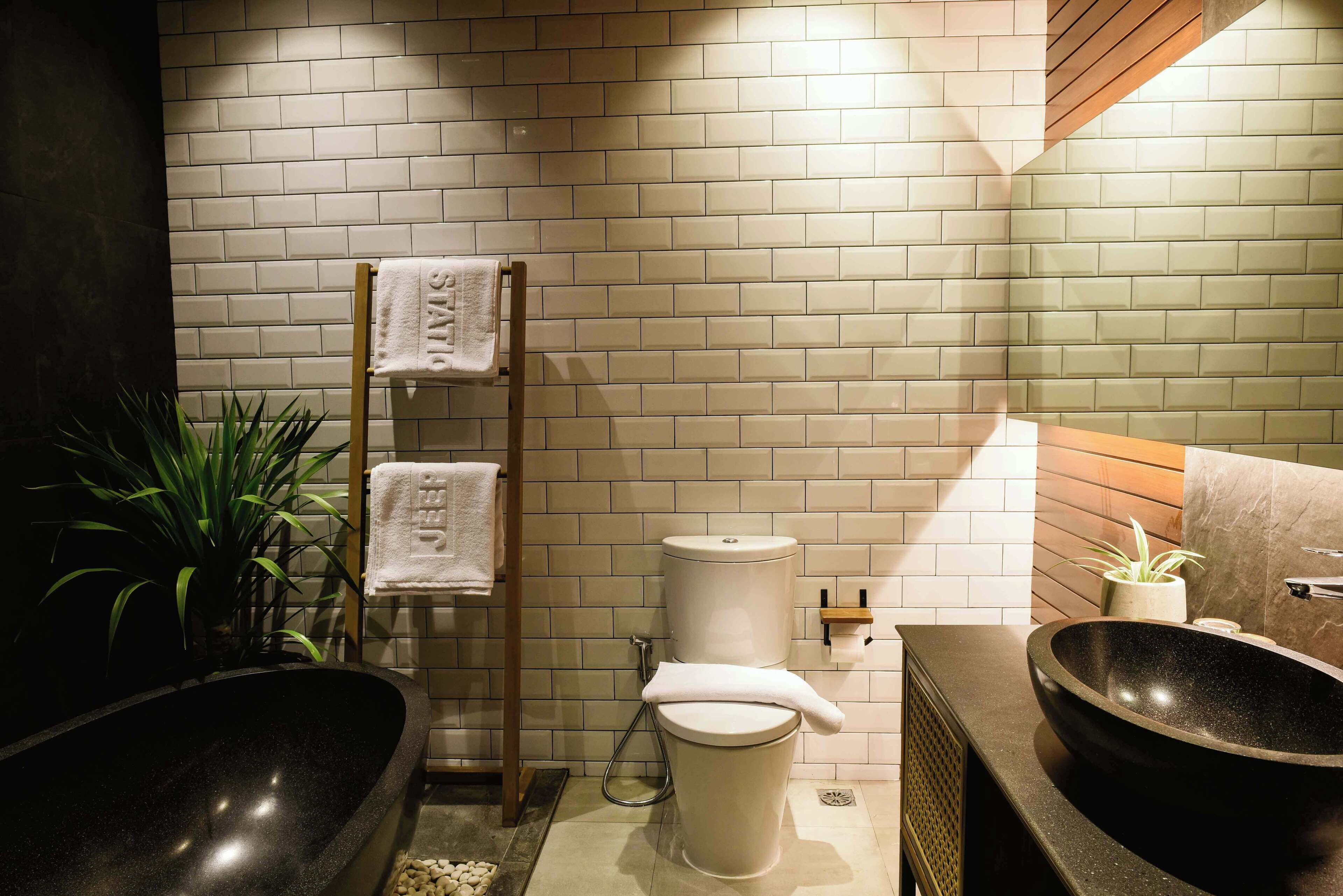 Een moderne badkamer met een zwart bad, een wit toilet en een houten handdoekrek.