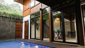 A modern house with a swimming pool, wooden exterior, and large glass doors leading to a dining area. - JSI Resort (Megamendung)