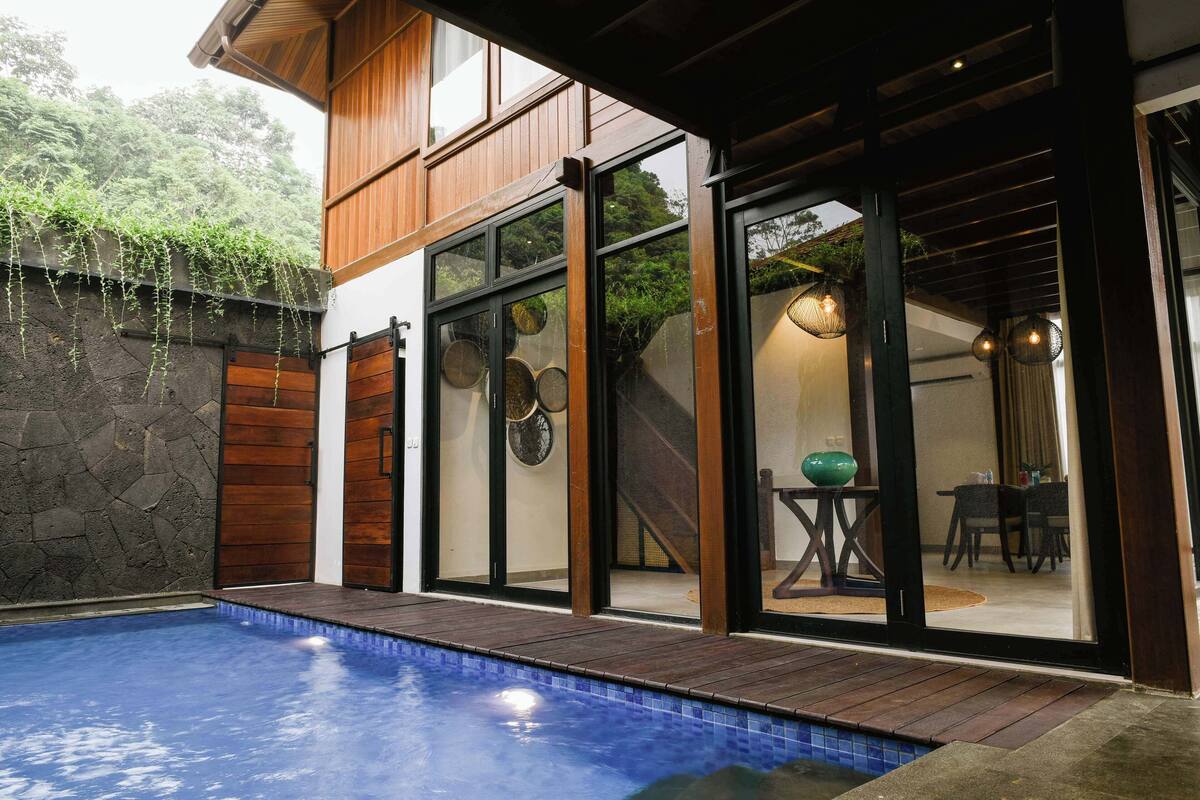 A modern house with a swimming pool, wooden exterior, and large glass doors leading to a dining area.
